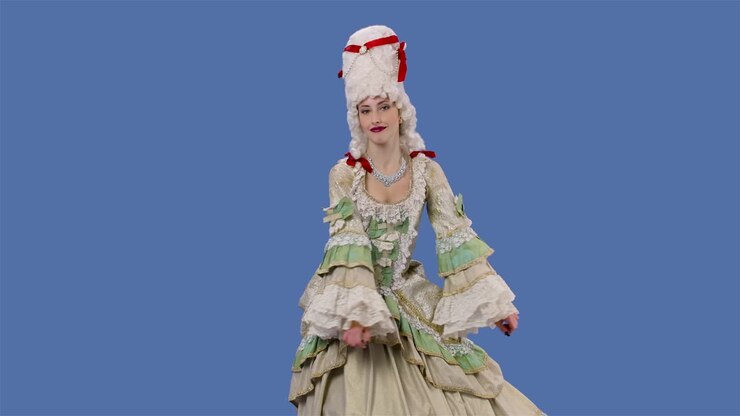 Ritratto di dama di corte in abito di pizzo vintage bianco e parrucca che balla allegramente. Giovane donna in posa in studio con sfondo a schermo blu. Movimento rallentato.