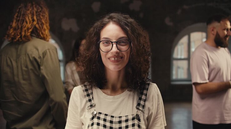 Portrait of a brunette girl with curly hair in round glasses who poses at group therapy in a brick building. Solving your problems and complexes in group therapy