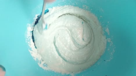 Mixing-blue-food-colouring-to-sponge-cake-batter-mixture-top-down-view-slow-motion