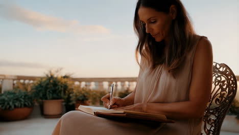 woman writing in a notebook on a patio at sunset