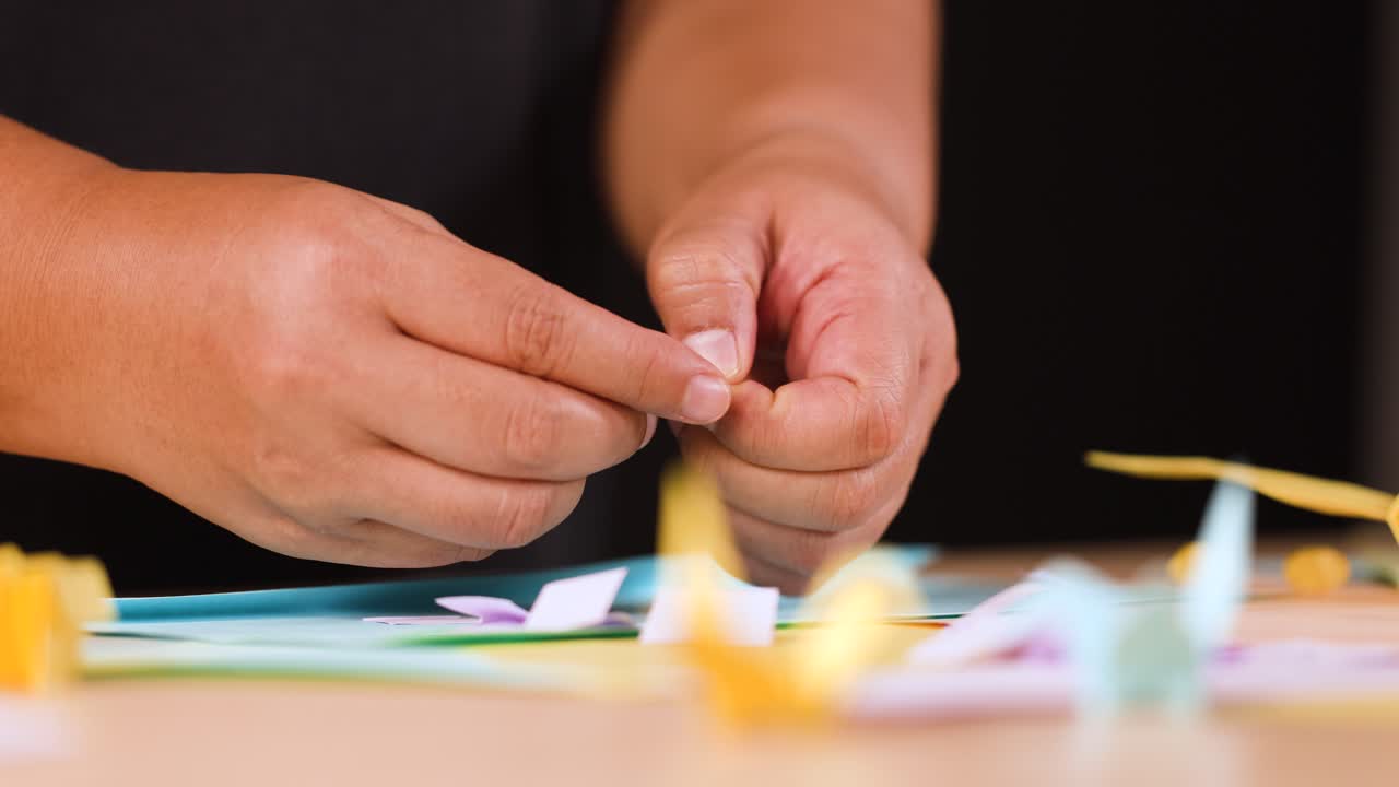 Primo piano di mani che piegano con cura un foglio di carta blu su un tavolo da lavoro in legno
