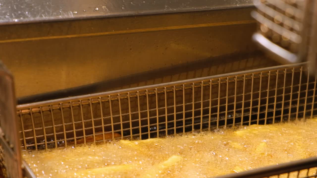 Nærbillede af pomfritter, der bobler i varm olie inde i en friturekurv