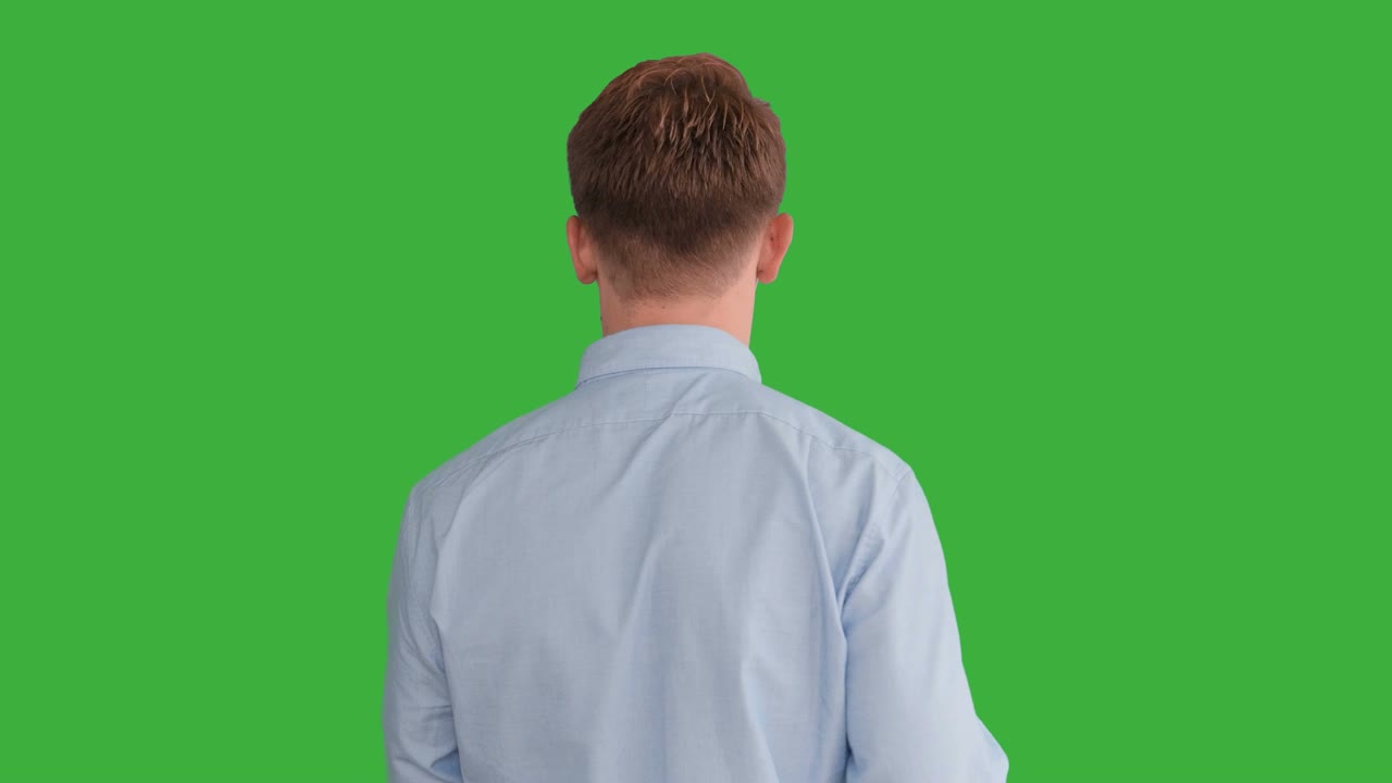 초록색 스크린 앞에서 연기하는 젊은 잘생긴 남성, 금발, 파란 셔츠, 파란 바지, 춤추고, 생각하고, 돌아서서 카메라와 대화합니다.