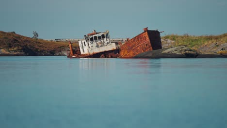 a rusty, abandoned shipwreck sunken near the rocky shores, with the calm waters and shoreline in the background