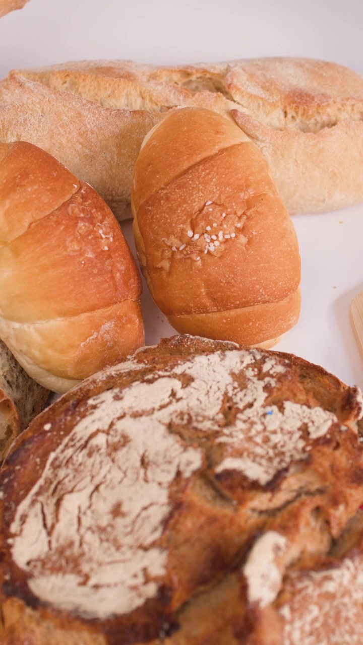 Hands slice crusty baguette on wooden board surrounded by sourdough loaves and golden croissants.