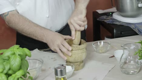 chef uses wooden pestle and mortar to grind up ingredients to make homemade pesto