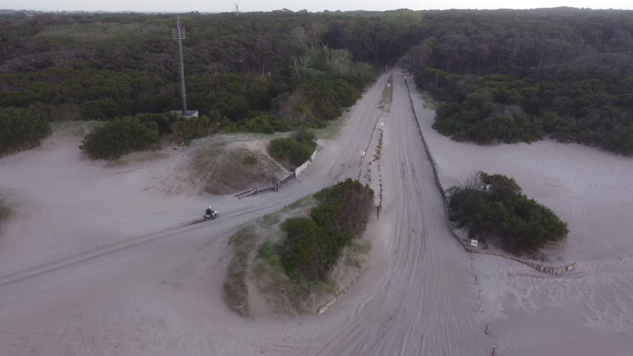 vista aérea de una persona conduciendo una moto en la arena de la playa en un fondo forestal en mar de las pampas, sudamérica