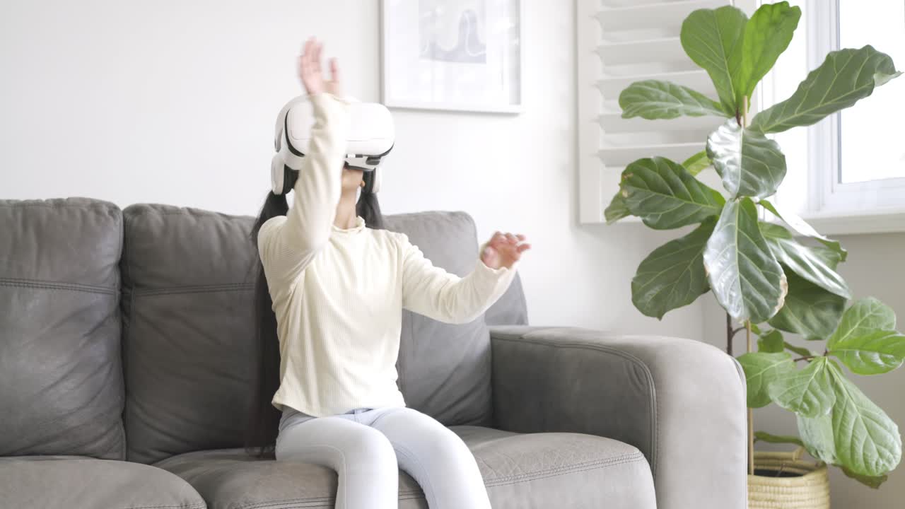 Joven estudiante recogiendo un visor de realidad virtual blanco, poniéndoselo sobre los ojos, explorando un mundo virtual en un sofá gris.