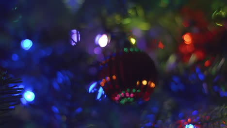 Panning-and-zooming-away-from-red-and-textured-bulb-ornament-with-steady,-multi-colored-bokeh-lights-on-a-Christmas-tree