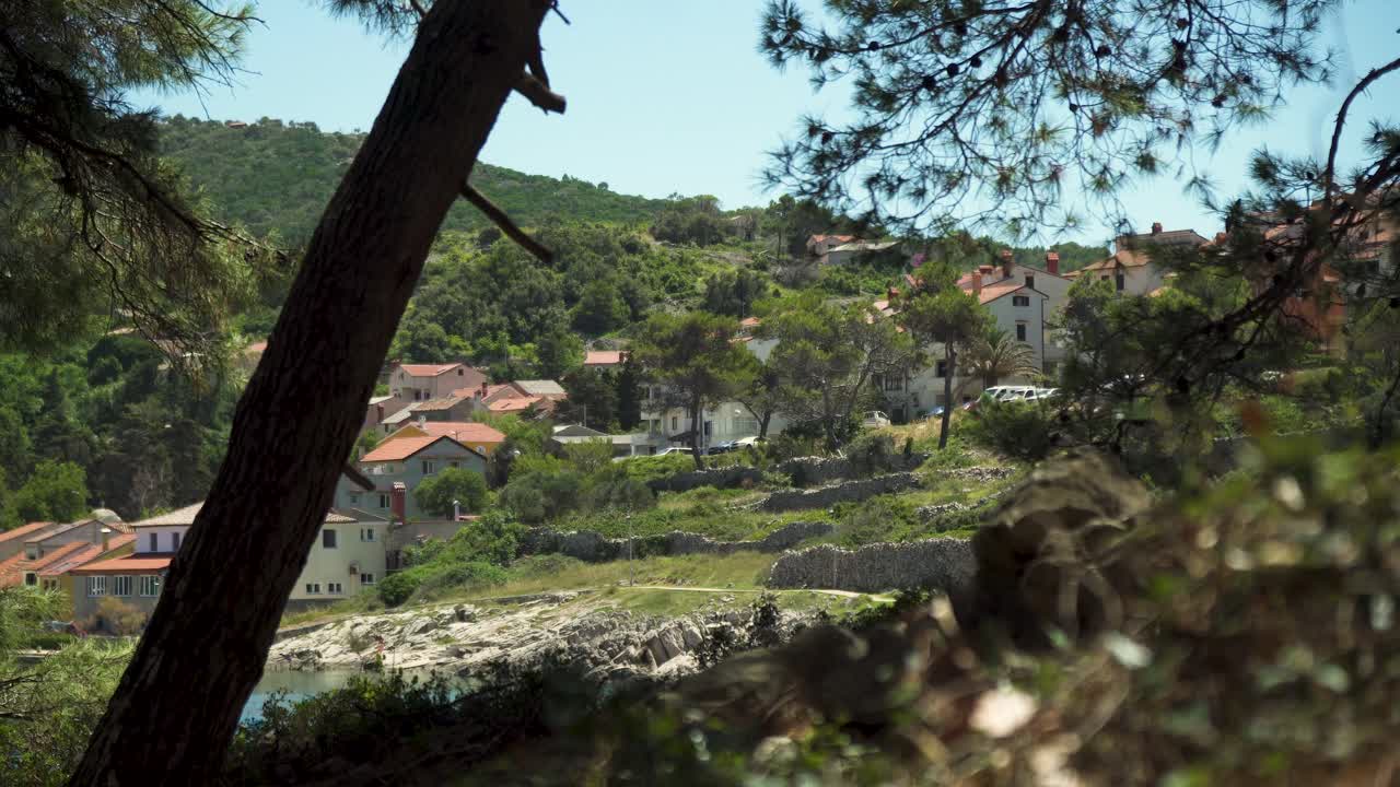 costa mediterránea con playa rocosa, casas con tejados rojos y paredes de piedra rodeadas de pinos