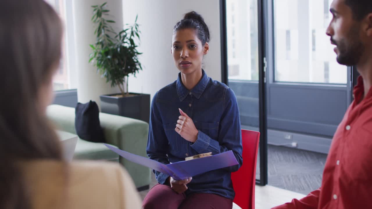 Mixed race businesswoman holding documents in a meeting with diverse group of colleagues