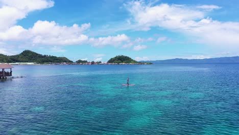 Männlicher-Tourist,-Der-Auf-Dem-Paddelbrett-Nahe-Den-Wasserhütten-Im-Tagbak-Marine-Park-Im-Südlichen-Leyte-Steht