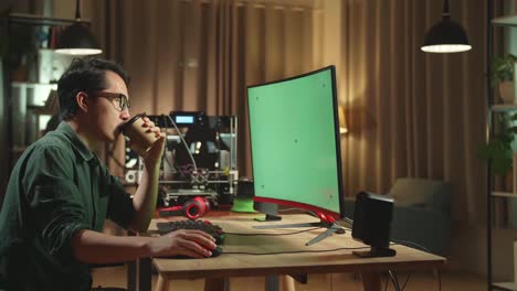 person working at a computer with a green screen display and drinking coffee