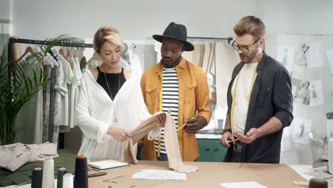 jóvenes y diseñadores de ropa trabajando juntos mientras una diseñadora elige una tela y se la muestra 2