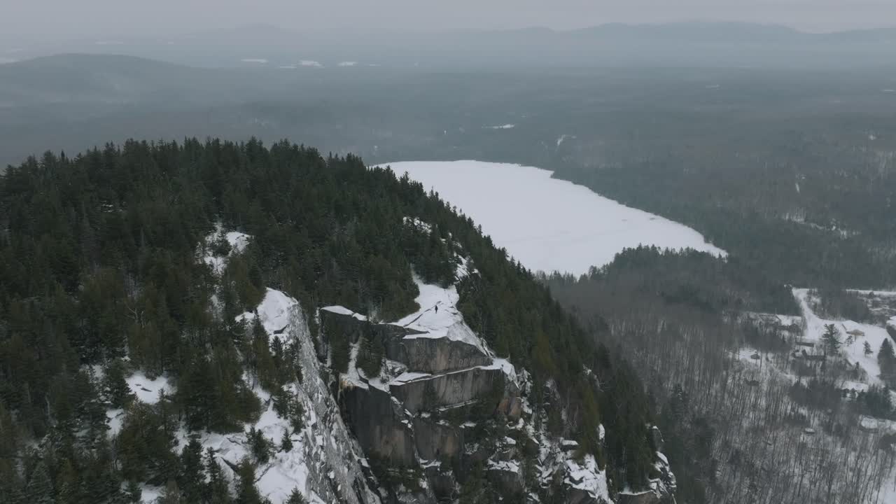 hombre en la cima de la montaña rocosa en la nieve con bosque de pinos durante el invierno en quebec, canadá