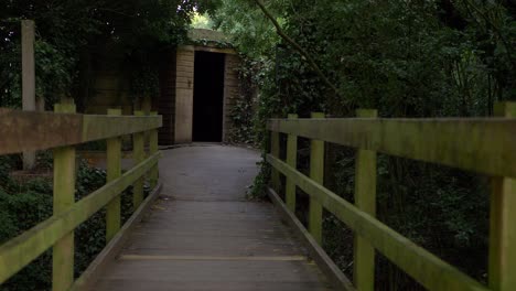 Walking-over-small-wooden-bridge-leading-to-a-doorway-wide-shot