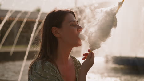 pretty lady eats sugar cotton wool against blurry fountain