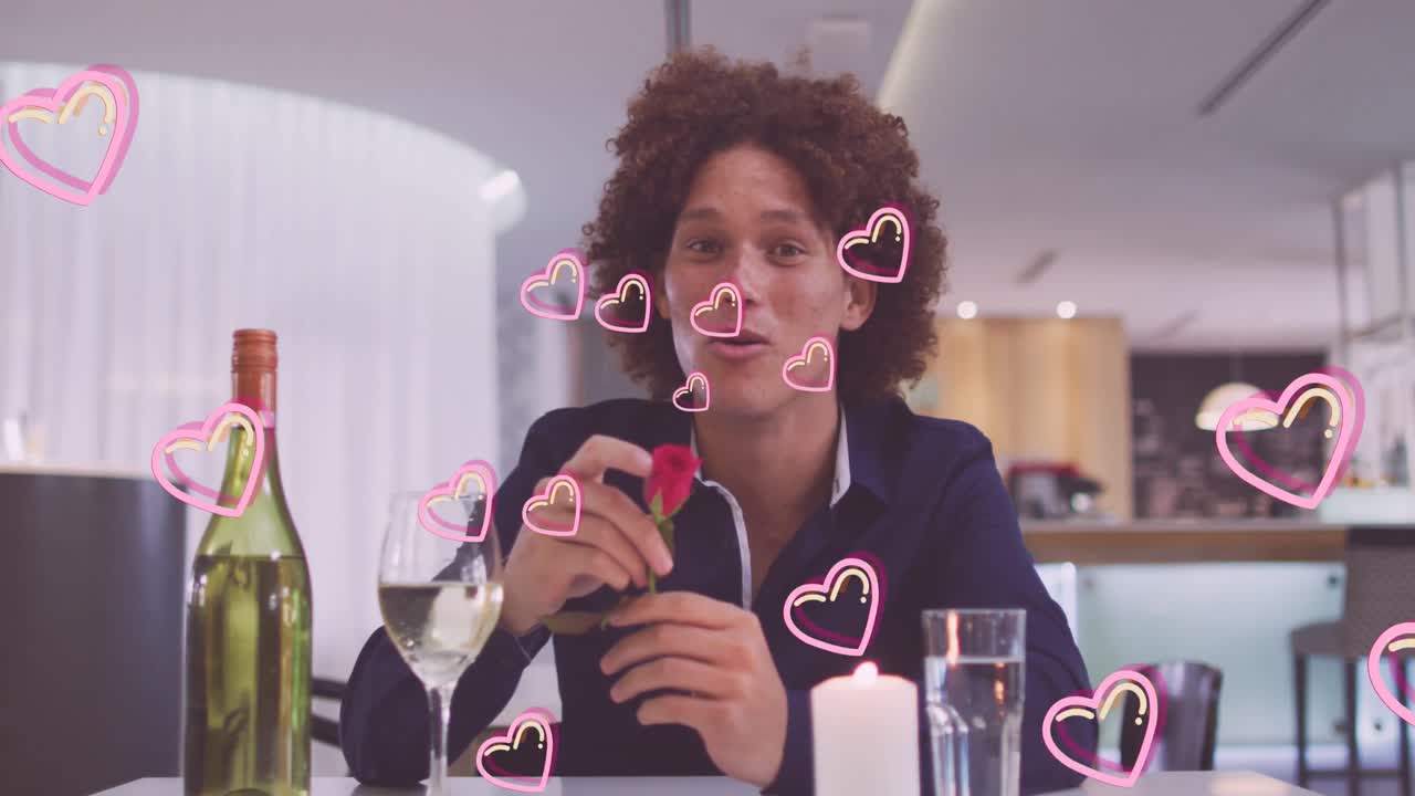 animación de iconos de corazón sobre feliz hombre biracial con vino teniendo videollamada