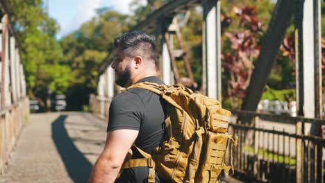 Traveler-with-backpack-walking-on-rusty-bridge-in-slow-motion-outdoors-on-sunny-summer-day-side-view