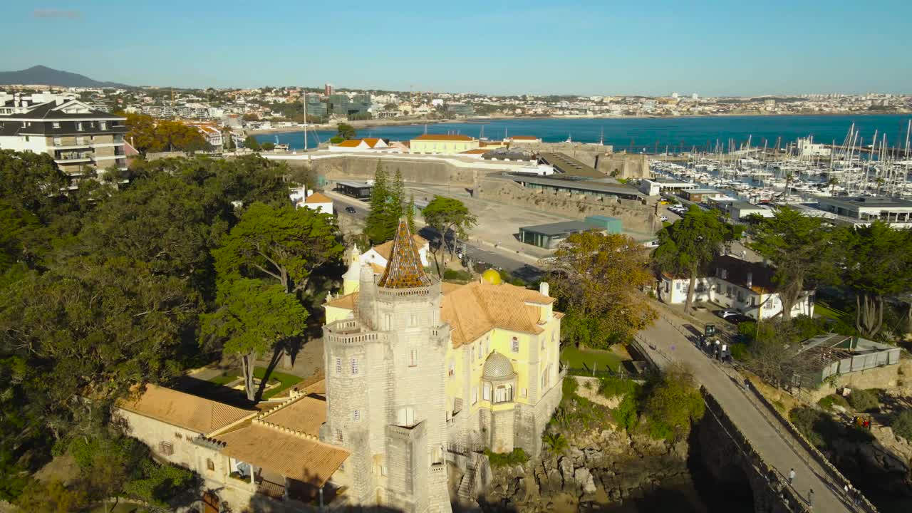 Órbita de dron de un histórico castillo costero con puerto deportivo y costa atlántica bajo la luz del sol.