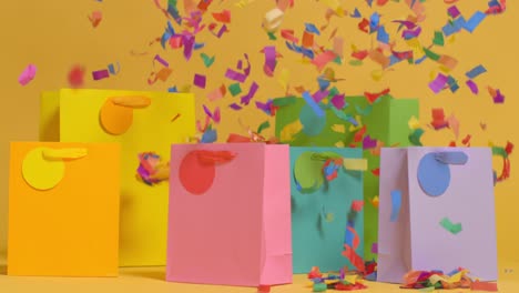 studio shot of colourful birthday party gift bags against yellow background with falling paper confetti 2