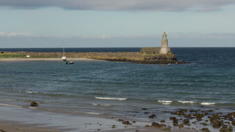 wide shot of port Logan harbour with old lighthouse and beach in foreground