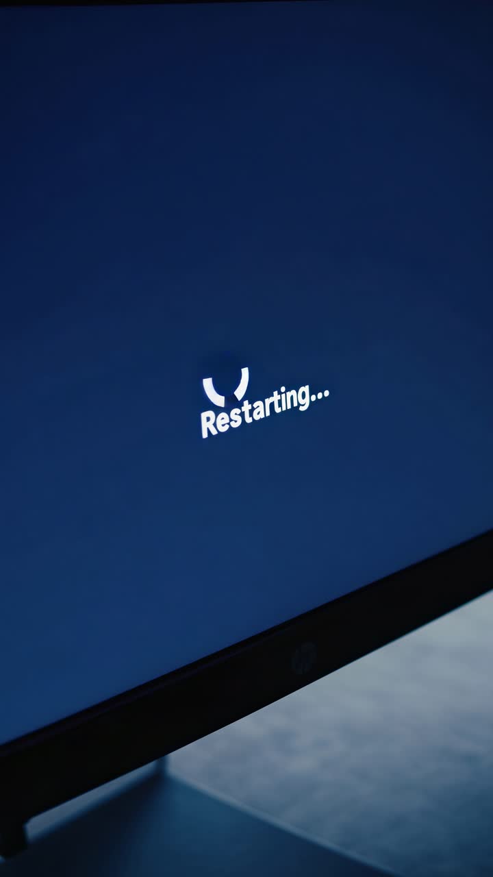 Close-up of a computer screen displaying 'Restarting...' in a dimly lit room, shot from a side