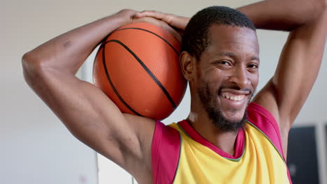 hombre afroamericano posa con una pelota de baloncesto en el gimnasio