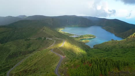 Vista-Aérea-Panorámica-Del-Lago-Lagoa-Do-Fogo-Rodeado-De-Exuberantes-Montañas-Verdes-Y-Caminos-Sinuosos