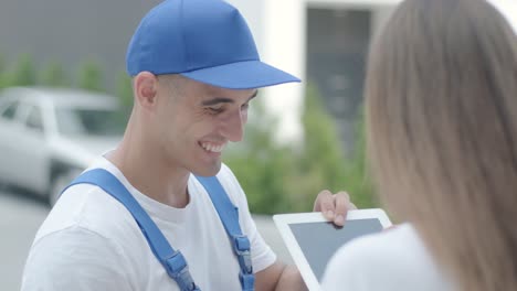 beautiful woman meets a delivery man who gives her a parcel box beside her home, she signs electronic signature on tablet. concept of courier, home delivery, online shopping