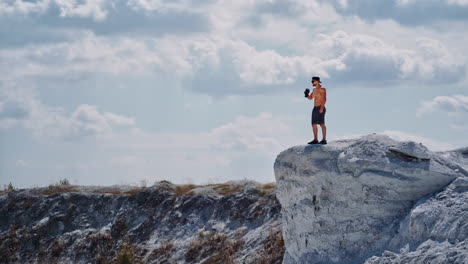 athlete drinking water on a white rock in summer. shirtless man with flask in white canyon in a sunny day. healthy sportsman after training outdoors.