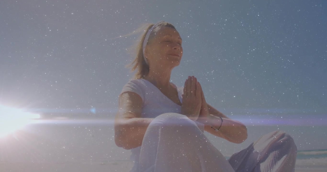 Mulher idosa levantando os braços na praia, unindo as mãos em posição de oração para bem-estar em meio a um reflexo de lente.