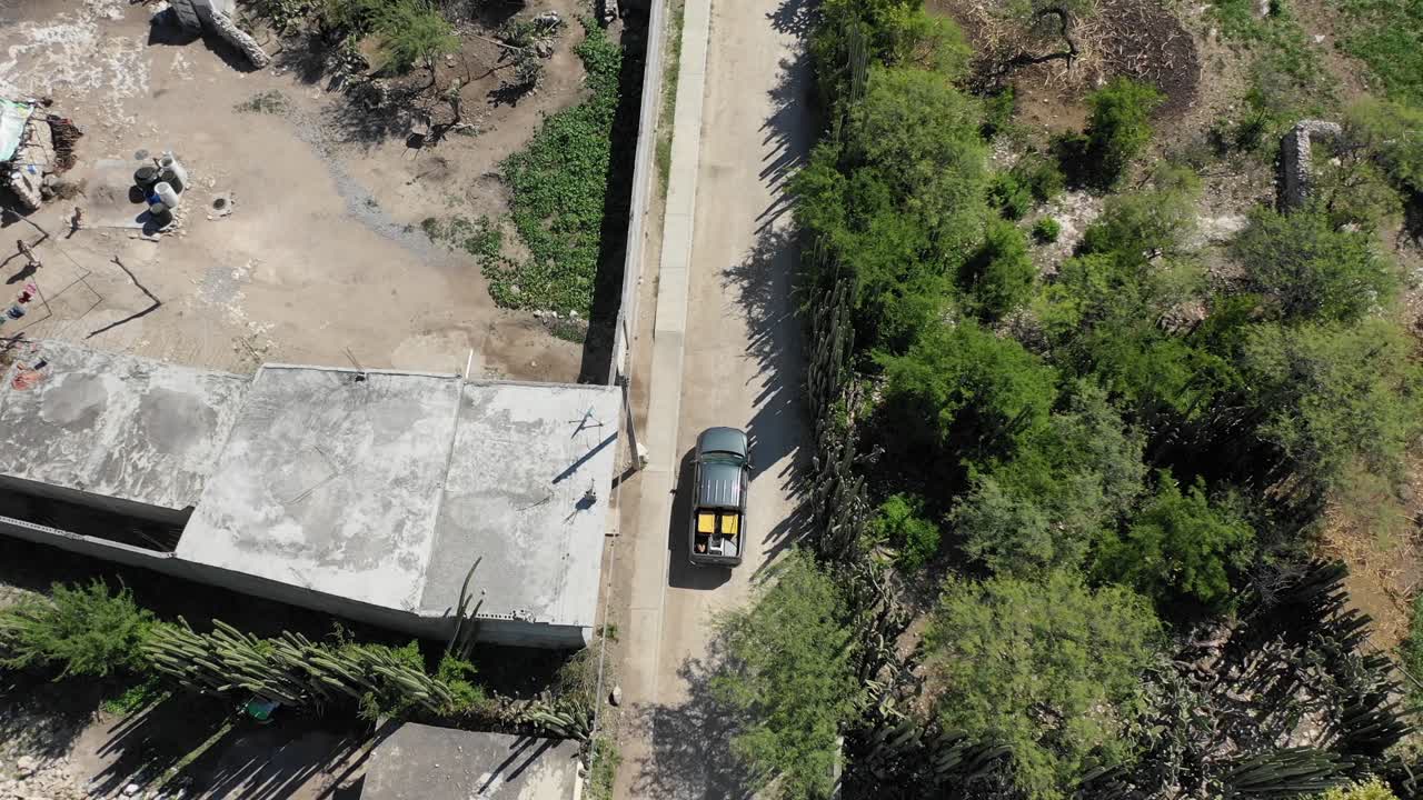 Desde arriba, una camioneta circula por un camino de tierra a través de un pueblo pobre en el desierto.