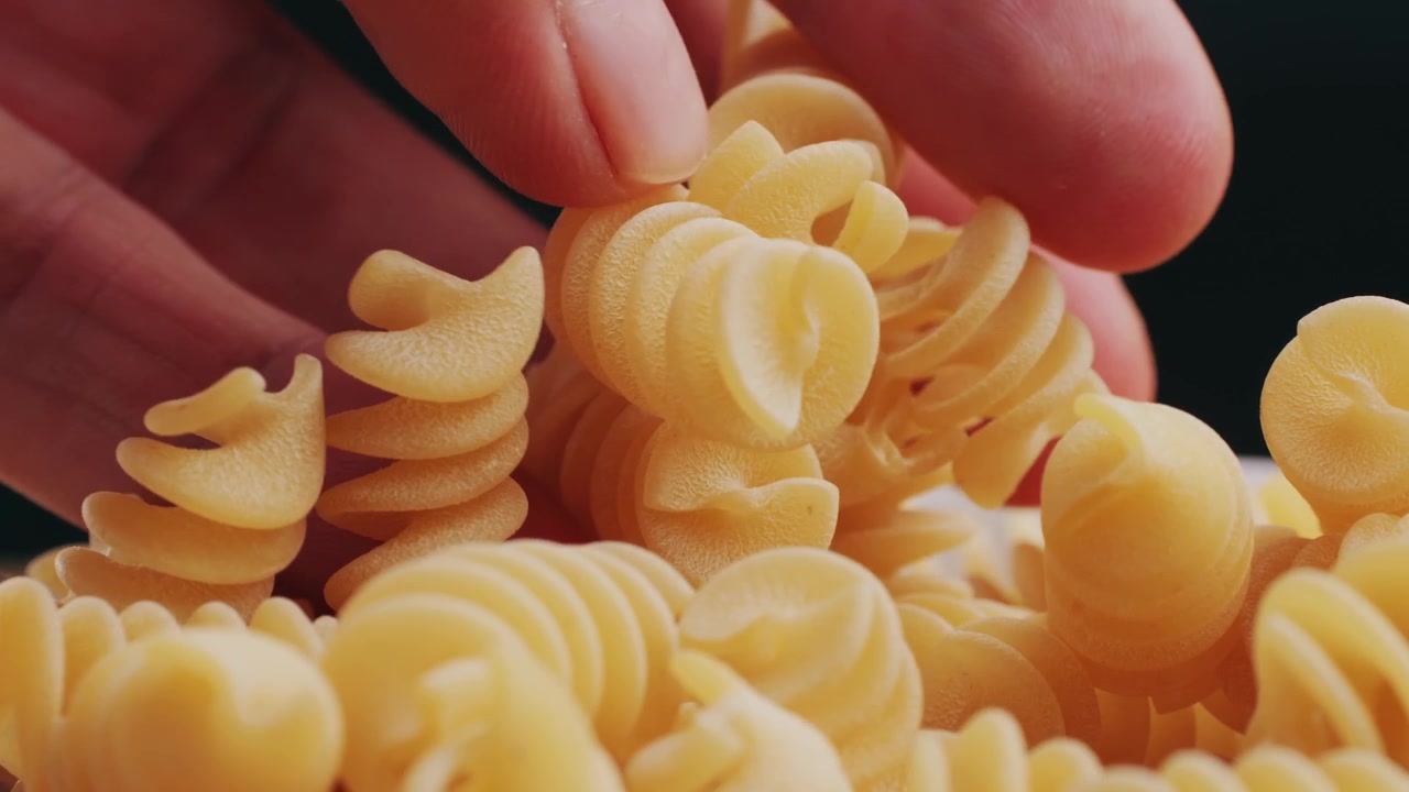Primo piano di una mano che raccoglie fusilli crudi
