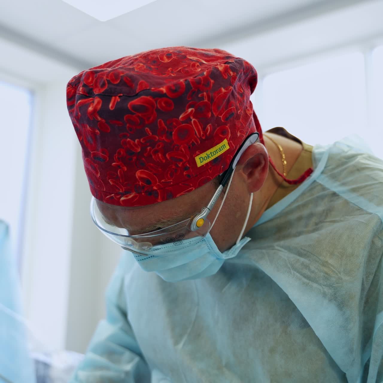 Male surgeon in red cap, mask, glasses and coat. Busy doctor working at operation in modern surgical room
