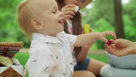 laughing toddler sitting on blanket with mother and sister in forest