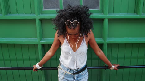 Young-black-woman-leaning-on-handrail-against-a-green-wall-in-city-street-laughing,-high-angle