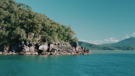 tropical rocky island with trees, tracking shot from boat