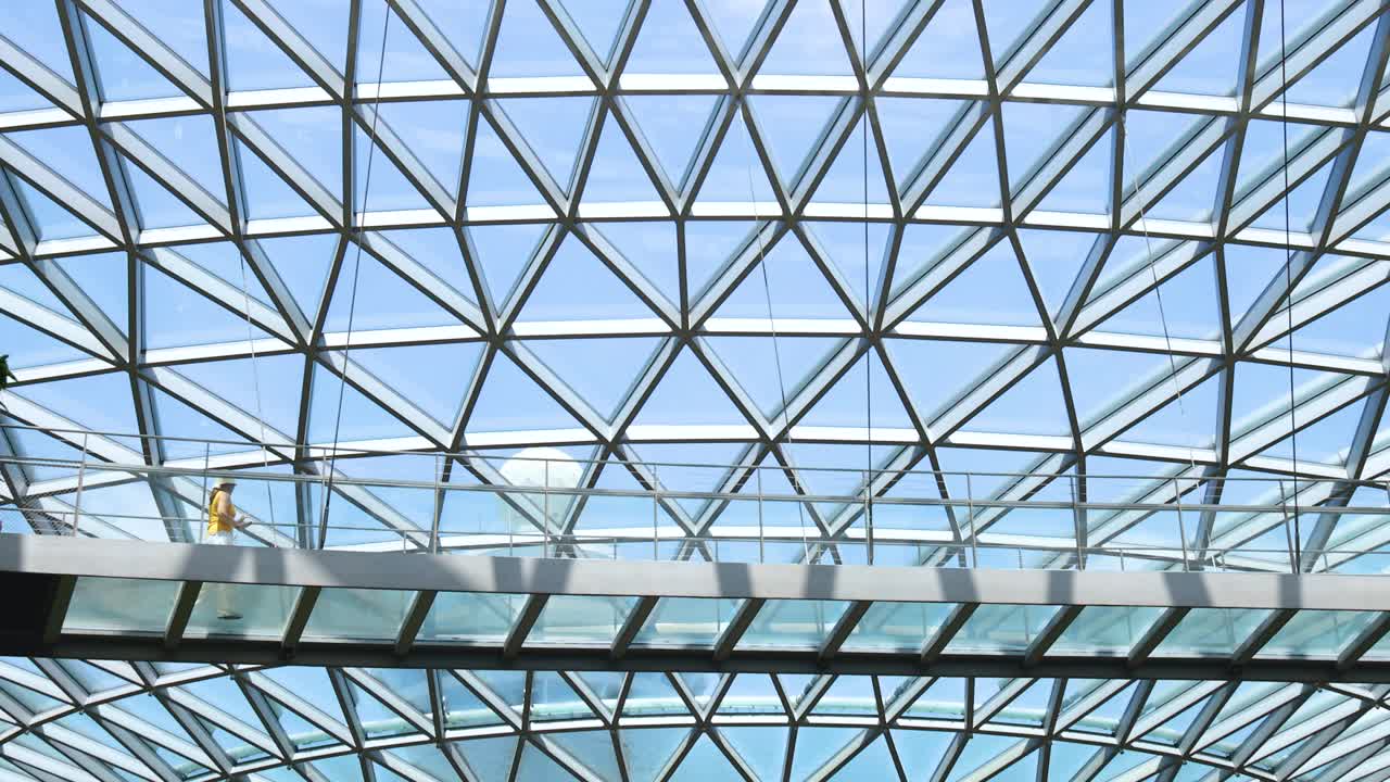 Camera tilts upward from lush indoor waterfall and greenery to expansive geometric glass dome ceiling, capturing bright daylight and modern architectural details