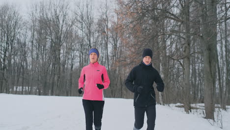 joven pareja familiar, hombre y mujer, corriendo por la mañana en el bosque de invierno. una mujer con una chaqueta holgada y un hombre con una chaqueta negra corre por un parque de invierno. estilo de vida saludable familia feliz