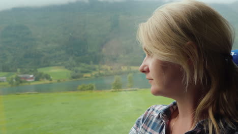 a woman travels by bus in norway looks out the window at the beautiful fjords