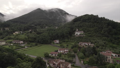 drone tiro de las nubes que se mueven más allá de la cámara en las colinas y montañas en italia en un día gris nublado con pueblos y casas en el suelo entre los campos verdes registro