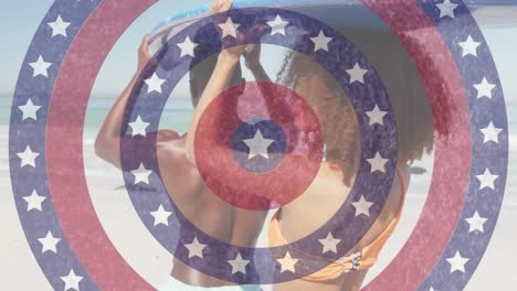 Animation-of-american-flag-circles-spinning-over-man-and-woman-carrying-surfboard-on-beach