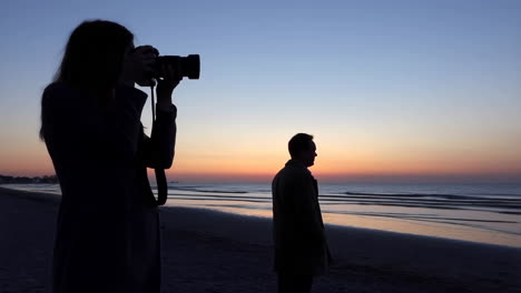 silhouettes of a photographer and a man on a beach at sunset