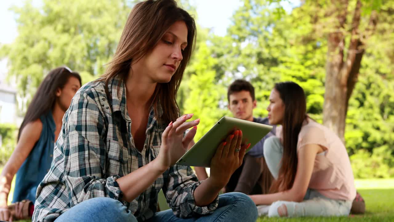 Student using tablet and classmates speaking behind her 