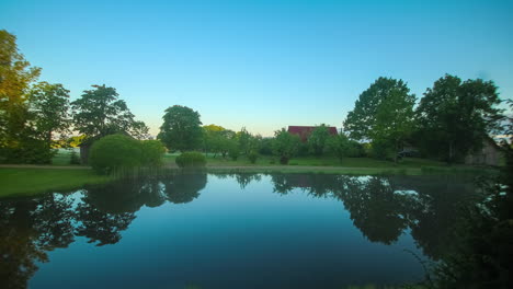 clouds in motion timelapse above an idyllic countryside lake and a red rooftop farmhouse in latvia