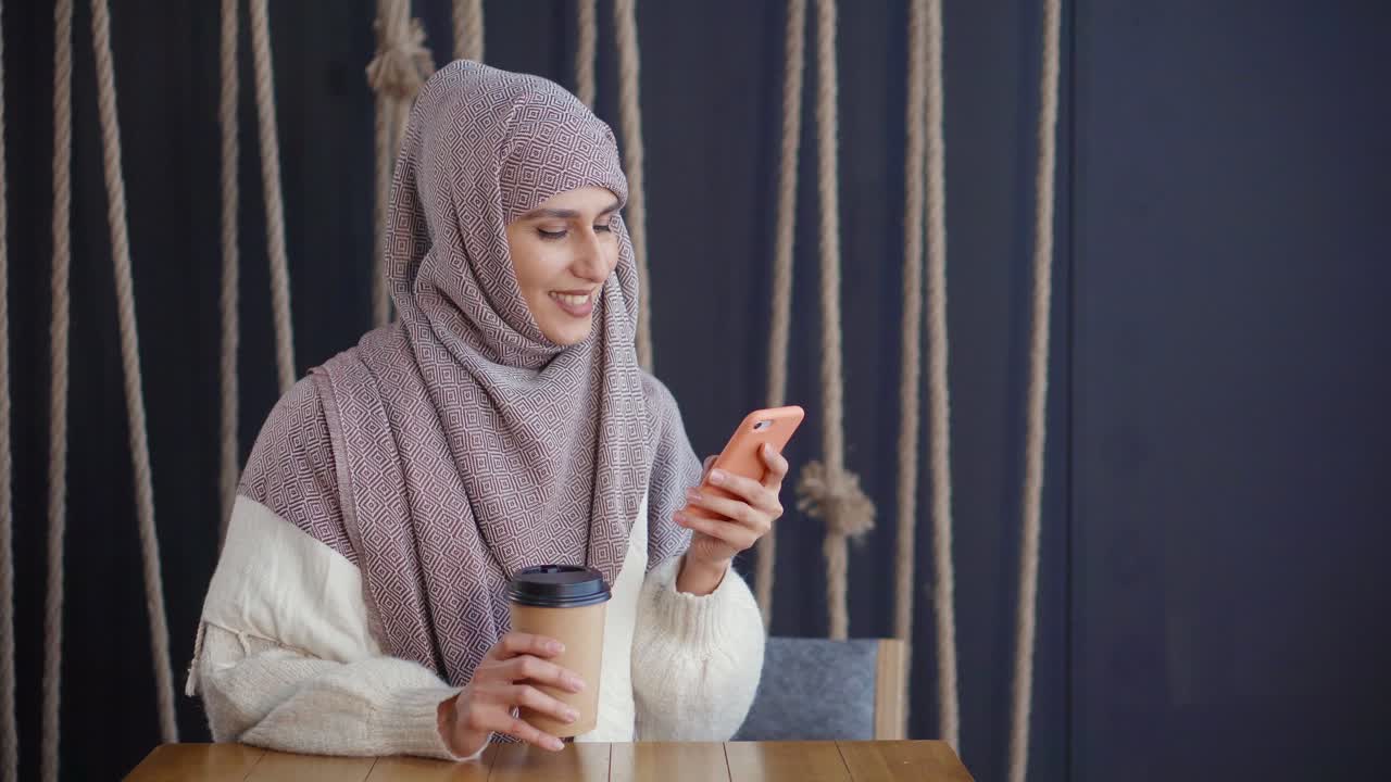 mujer en hijab usando un teléfono inteligente en un café