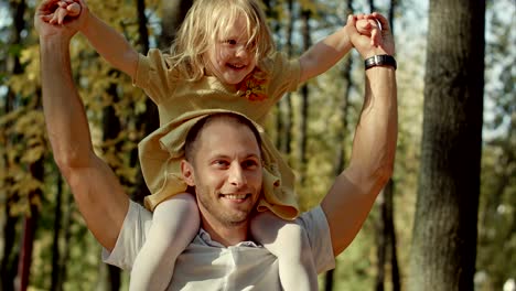 little girl riding on dads neck at autumn park