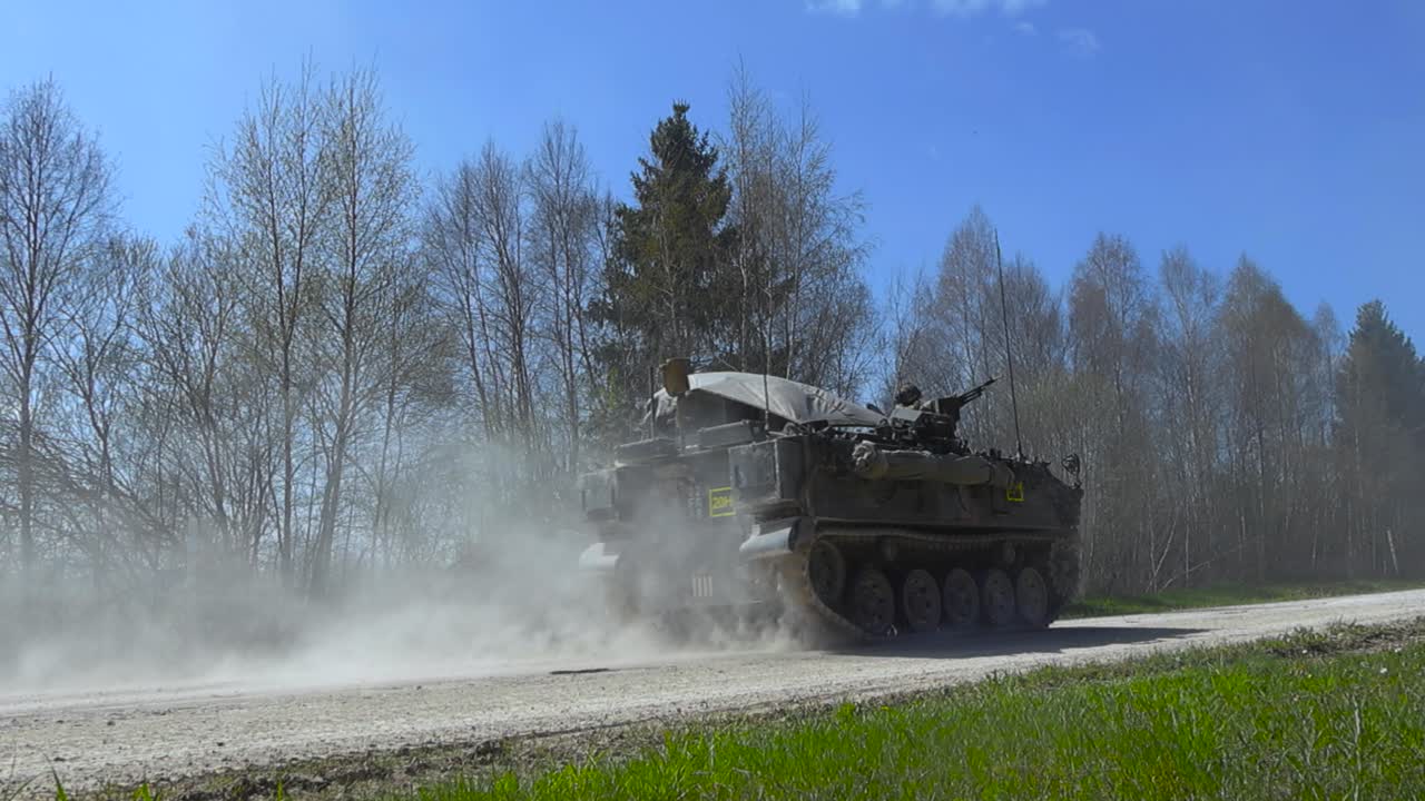 Rare awesome military footage of a FV432 armoured vehilve with infanrty on it driving by on a dusty white countryside road in a ummer sunny forest during an battle exercise called SIIL 2025, slow-mo.