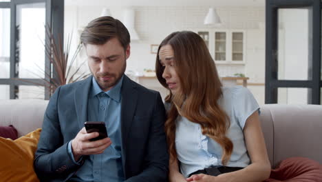 una pareja de negocios relajándose en el sofá juntos. una mujer molesta mirando al teléfono del hombre